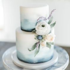 a white and blue wedding cake with flowers on the top is sitting on a plate