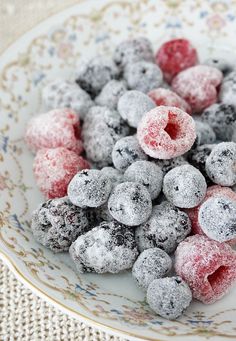 a white plate topped with powdered donuts covered in raspberries and blueberries