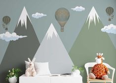 a child's room with mountains and hot air balloons painted on the wall, including a giraffe stuffed animal