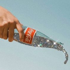 a hand holding a coca - cola bottle in the air with sparkling glitters on it