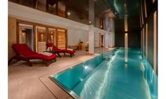 an indoor swimming pool with chaise lounges next to it and two red chairs