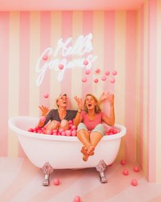 two women sitting in a bathtub with pink balls all over the floor and walls