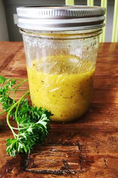 a jar filled with yellow liquid sitting on top of a wooden table next to a sprig of parsley