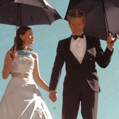 two people dressed in formal wear holding umbrellas