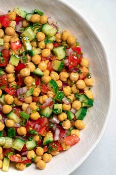 a white bowl filled with chickpeas, cucumber and red onion salad