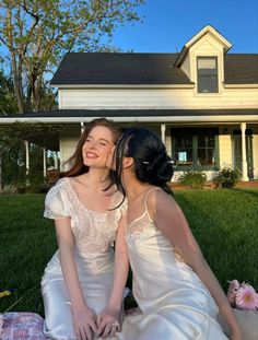 two women sitting on the grass in front of a house