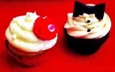 two cupcakes with white frosting and black bows are on a red surface