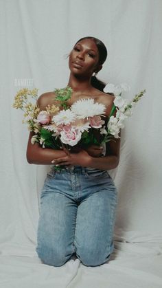 a woman sitting on the ground with flowers in her lap and one arm around her body