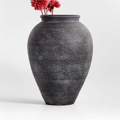 a black vase with flowers in it on a white background, the image appears to have been altered