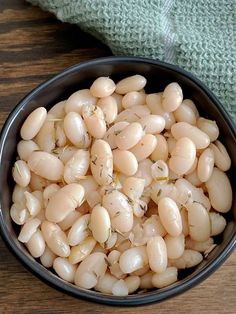 a black bowl filled with white beans on top of a wooden table next to a green towel