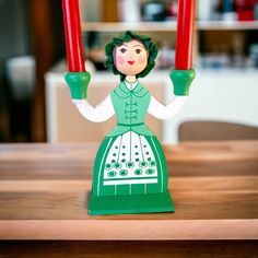 a figurine holding two red candles on top of a wooden table