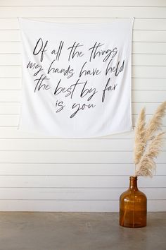 a white wall hanging on the side of a building next to a vase with dry grass in it