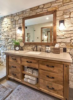 a bathroom with stone wall and wooden cabinets, mirror above the sink, rugs on the floor