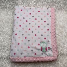 a pink and green polka dot blanket with a small stuffed animal on the bottom corner