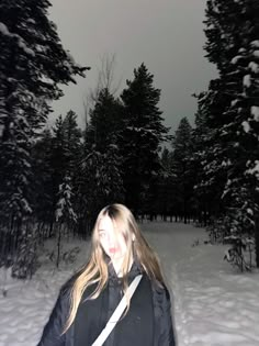 a woman standing in the snow with trees behind her