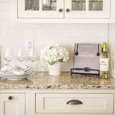 a kitchen counter with white cabinets and wine glasses