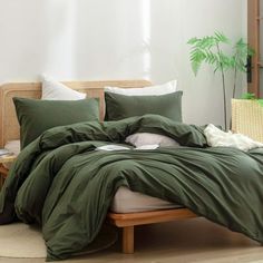 a bed with green sheets and pillows in a room next to a plant on the floor