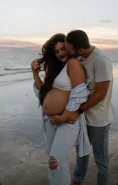 a man and woman standing next to each other on the beach with their belly wrapped up