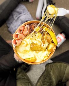 a person holding a bowl filled with food and eating utensils in it's hands