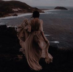 a woman in a long dress is walking along the ocean shore with her back to the camera