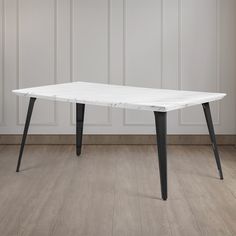 a white marble dining table with black metal legs on a wooden floor in an empty room