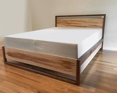 a bed with wooden headboard and foot board on hardwood flooring in an empty room