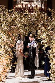 a bride and groom standing in front of an arch with flowers on it at their wedding ceremony