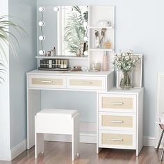 a white dressing table with drawers, mirror and stool next to a potted plant