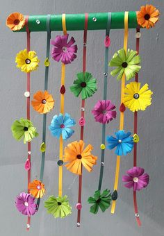 colorful paper flowers are hanging from a green string on the wall in front of a gray wall