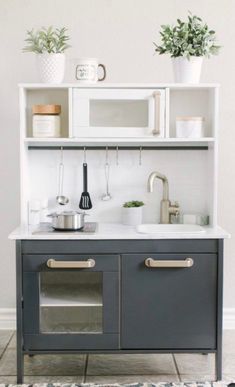 a kitchen with white cabinets and gray counter tops, potted plants on the shelf