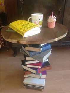 a stack of books sitting on top of a wooden table next to a cup with a candle