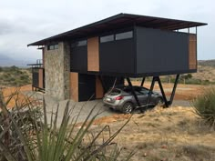 a car is parked in front of a small house on stilts that have been built into the ground