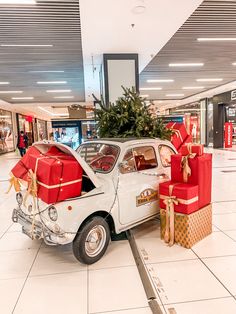 an old car with presents on the back in a shopping mall parking lot next to a christmas tree