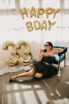 a woman in a black dress sitting on a blue chair with the number 35 balloon behind her