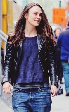 a woman walking down the street with her hand in her pocket and wearing a black leather jacket