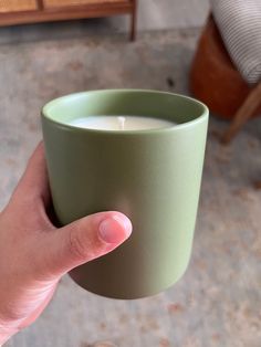 a person holding a green cup with a white candle in it's middle and their left hand