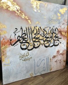 a painting with arabic writing on it sitting on top of a wooden floor next to a wall