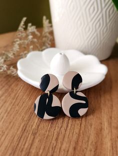 two black and white earrings sitting on top of a wooden table next to a vase