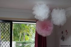 three fluffy pink and white pom - poms hanging from the ceiling in front of a window