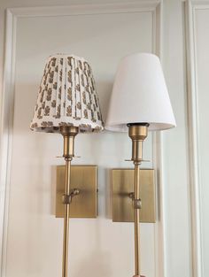 a pair of wall lights with a lamp shade on each one and a hand holding the light