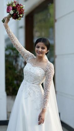 a woman in a white wedding dress holding up her bouquet and smiling at the camera