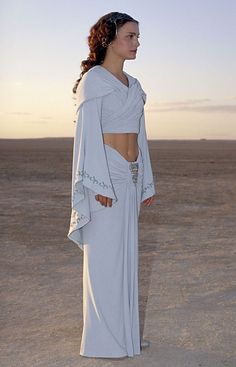 a woman standing in the desert wearing a white dress with cutouts on it's sides