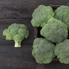 several pieces of broccoli in a basket on a wooden table with other vegetables