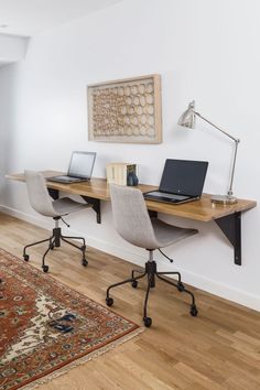 two laptops are sitting on the desk in front of a large rug and lamp