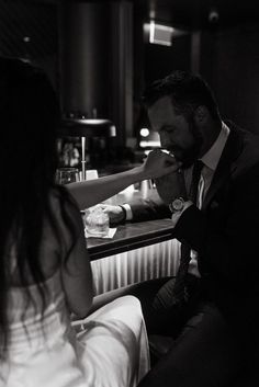 a man in a suit sitting at a bar with his hand on the woman's mouth