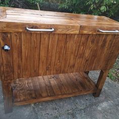 a wooden cabinet sitting on top of a stone floor next to trees and bushes in the background