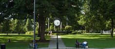 people sitting on benches in the middle of a park with a large clock above them