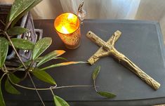 a cross and candle on a table next to a plant in a glass vase with leaves