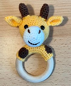 a crocheted giraffe toy hanging from a wooden ring on a table