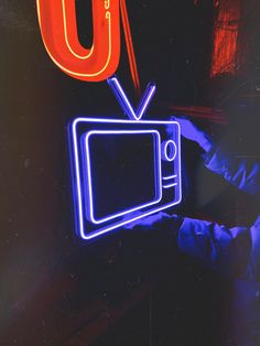 a person holding up a neon sign in front of a tv set with the letter u on it